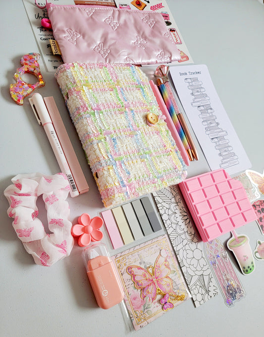 Christmas Bookish Bundle flatlay featuring pastel stationery gifts: A6 tweed notebook, pink pencil case, kawaii pens, book tracker, sticky notes, scrunchie, acrylic bookmarks, butterfly stickers, and planner accessories. Aesthetic pastel holiday gift set, perfect for readers, journaling lovers, stocking stuffers, and Secret Santa Christmas presents