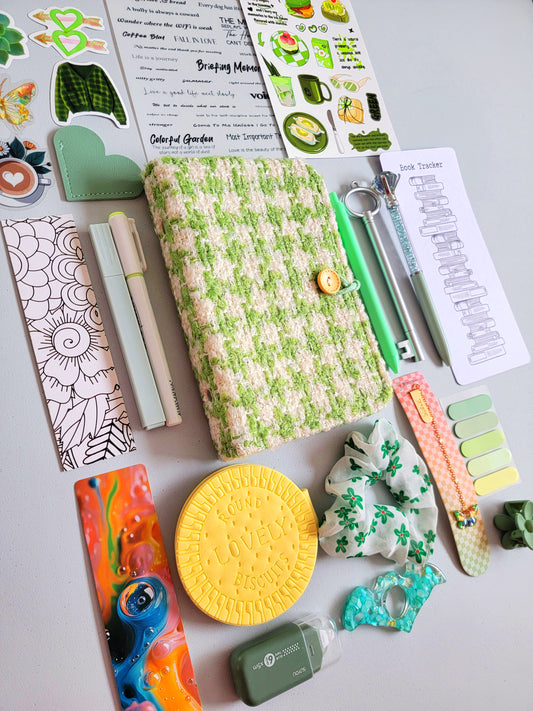 Green aesthetic bookish holiday gift bundle flatlay featuring a green tweed notebook cover, pastel green pens, book tracker, stickers, bookmarks, scrunchie, page tabs, pencil sharpener, and cute stationery accessories. A cozy Christmas gift set for book lovers, students, and journaling enthusiasts.