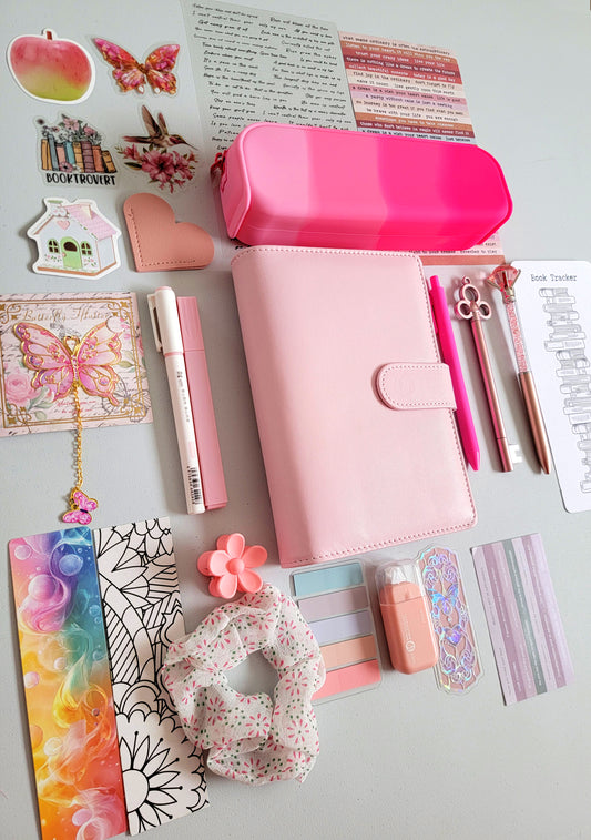 Pink aesthetic bookish holiday gift bundle flatlay featuring a pastel pink planner cover, hot pink gradient pencil case, book tracker, pink pens, butterfly charm, decorative stickers, bookmarks, scrunchie, pastel page tabs and cute stationery accessories. A charming Christmas gift set for book lovers, journalers and students.