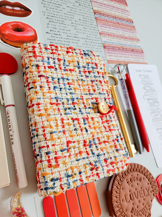Red aesthetic bookish holiday gift bundle flatlay featuring a red-tweed notebook cover, book tracker, red and gold pens, stickers, bookmarks, tabs, scrunchie, cute stationery accessories, and a biscuit-shaped pouch. A cozy Christmas gift set for book lovers, journaling enthusiasts, and students.