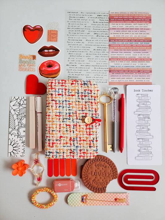 Red aesthetic bookish holiday gift bundle flatlay featuring a red-tweed notebook cover, book tracker, red and gold pens, stickers, bookmarks, tabs, scrunchie, cute stationery accessories, and a biscuit-shaped pouch. A cozy Christmas gift set for book lovers, journaling enthusiasts, and students.