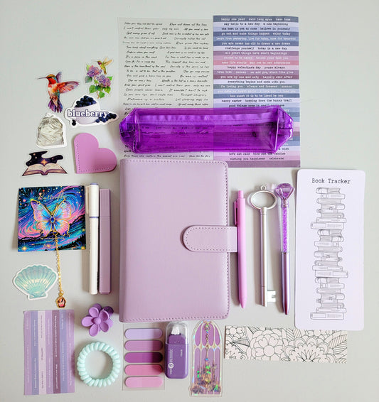 Purple and lilac aesthetic bookish holiday gift bundle flatlay featuring a lavender planner cover, transparent purple pencil case, book tracker, pastel purple pens, stickers, bookmarks, scrunchie, tabs, and cute stationery accessories. A cozy Christmas gift set for book lovers, journalers, and students.