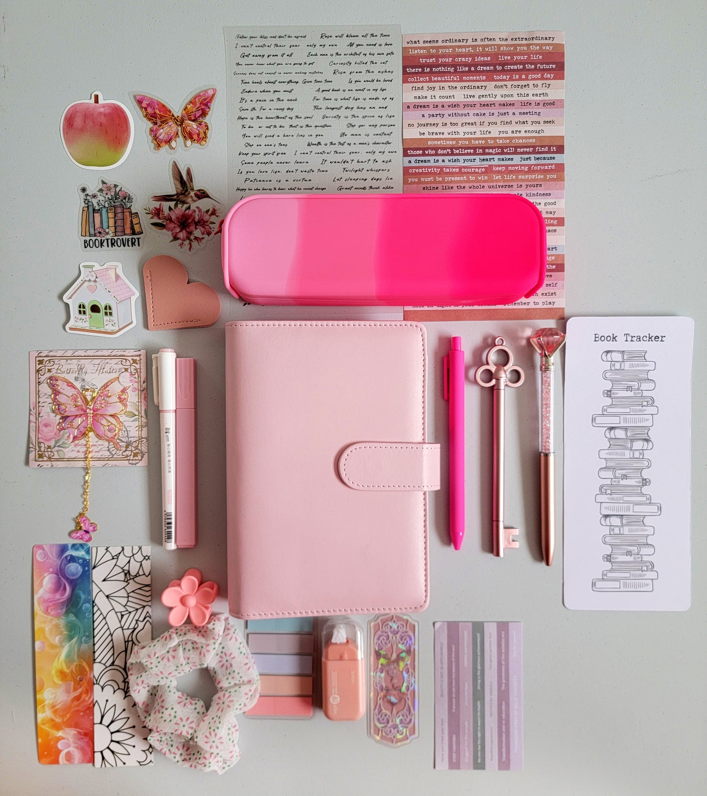 Pink aesthetic bookish holiday gift bundle flatlay featuring a pastel pink planner cover, hot pink gradient pencil case, book tracker, pink pens, butterfly charm, decorative stickers, bookmarks, scrunchie, pastel page tabs and cute stationery accessories. A charming Christmas gift set for book lovers, journalers and students.