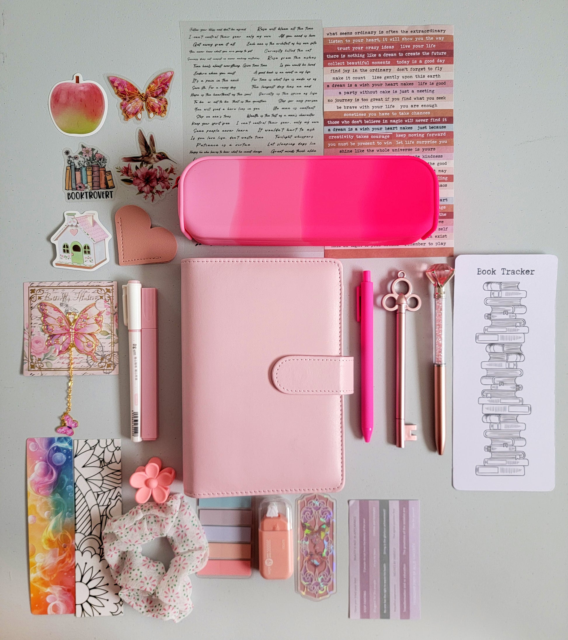 Pink aesthetic bookish holiday gift bundle flatlay featuring a pastel pink planner cover, hot pink gradient pencil case, book tracker, pink pens, butterfly charm, decorative stickers, bookmarks, scrunchie, pastel page tabs and cute stationery accessories. A charming Christmas gift set for book lovers, journalers and students.