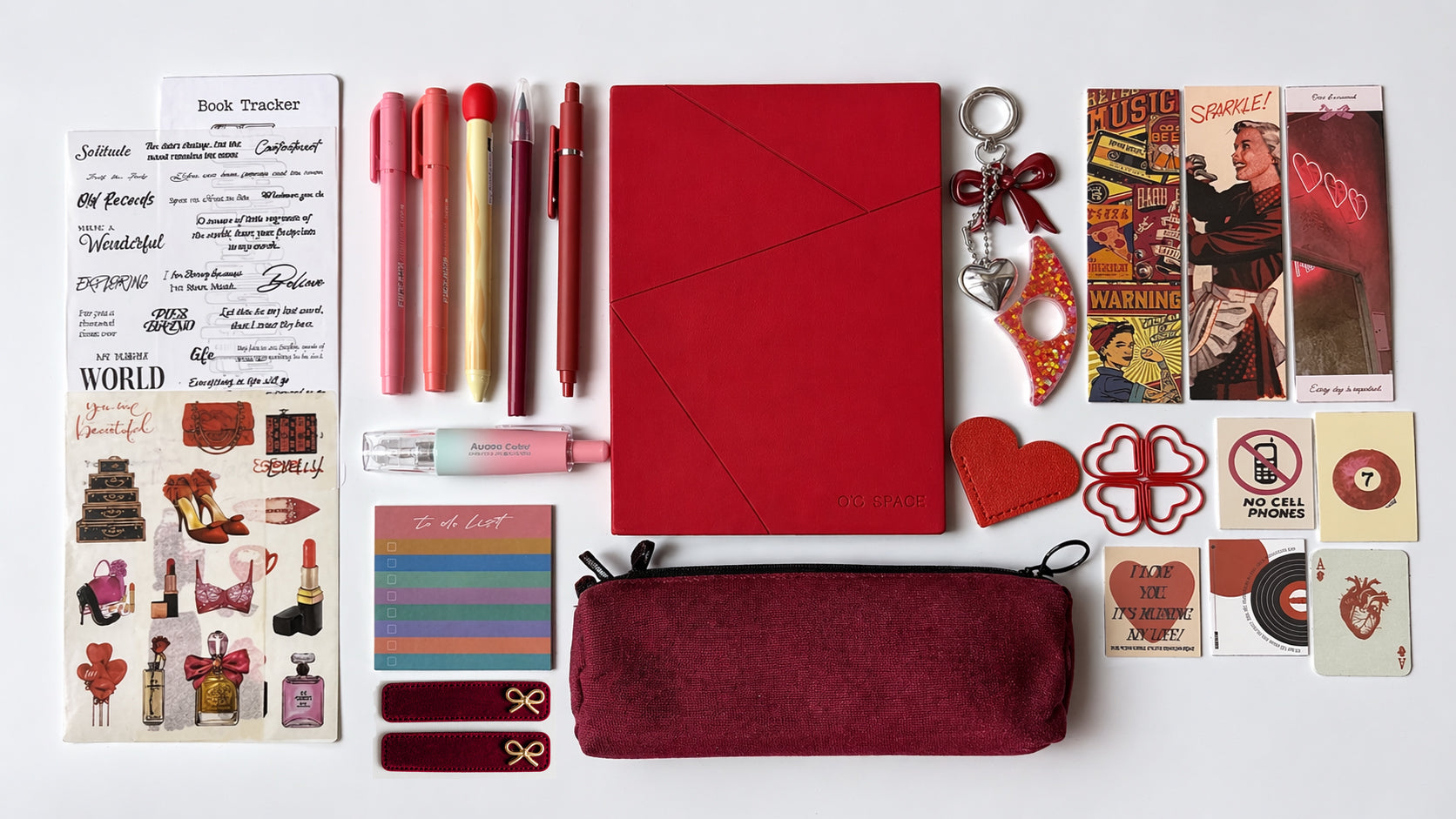 Collection of stationery items including a red notebook, pens, a pencil case, and decorative elements on a white background.