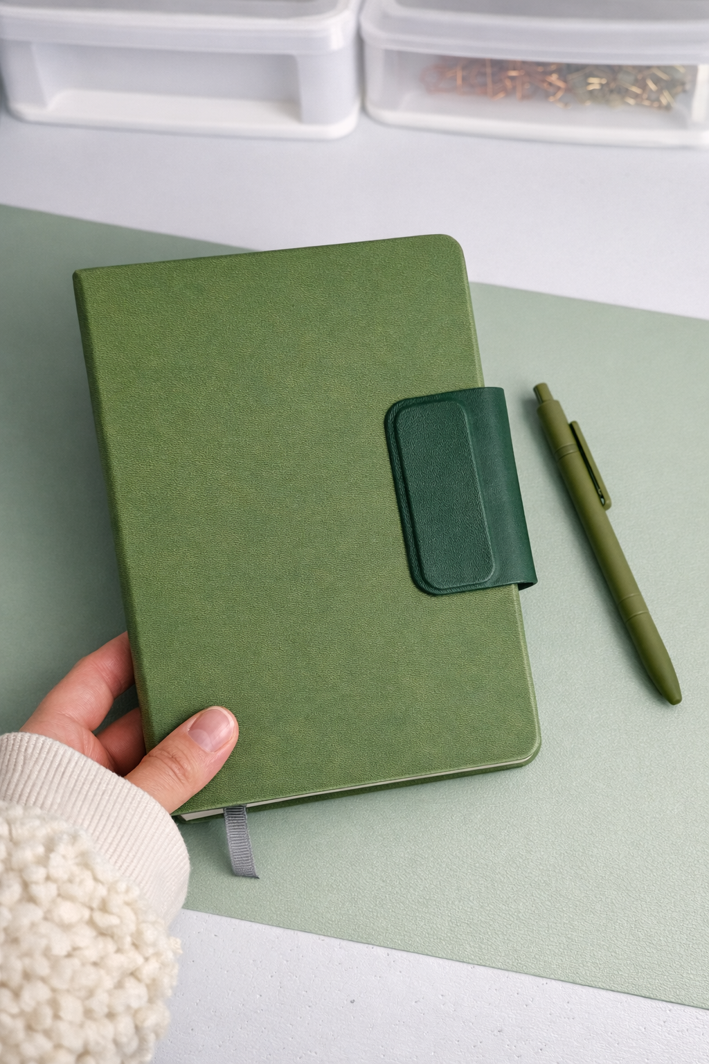Green notebook with a pen holder and pen on a light green surface